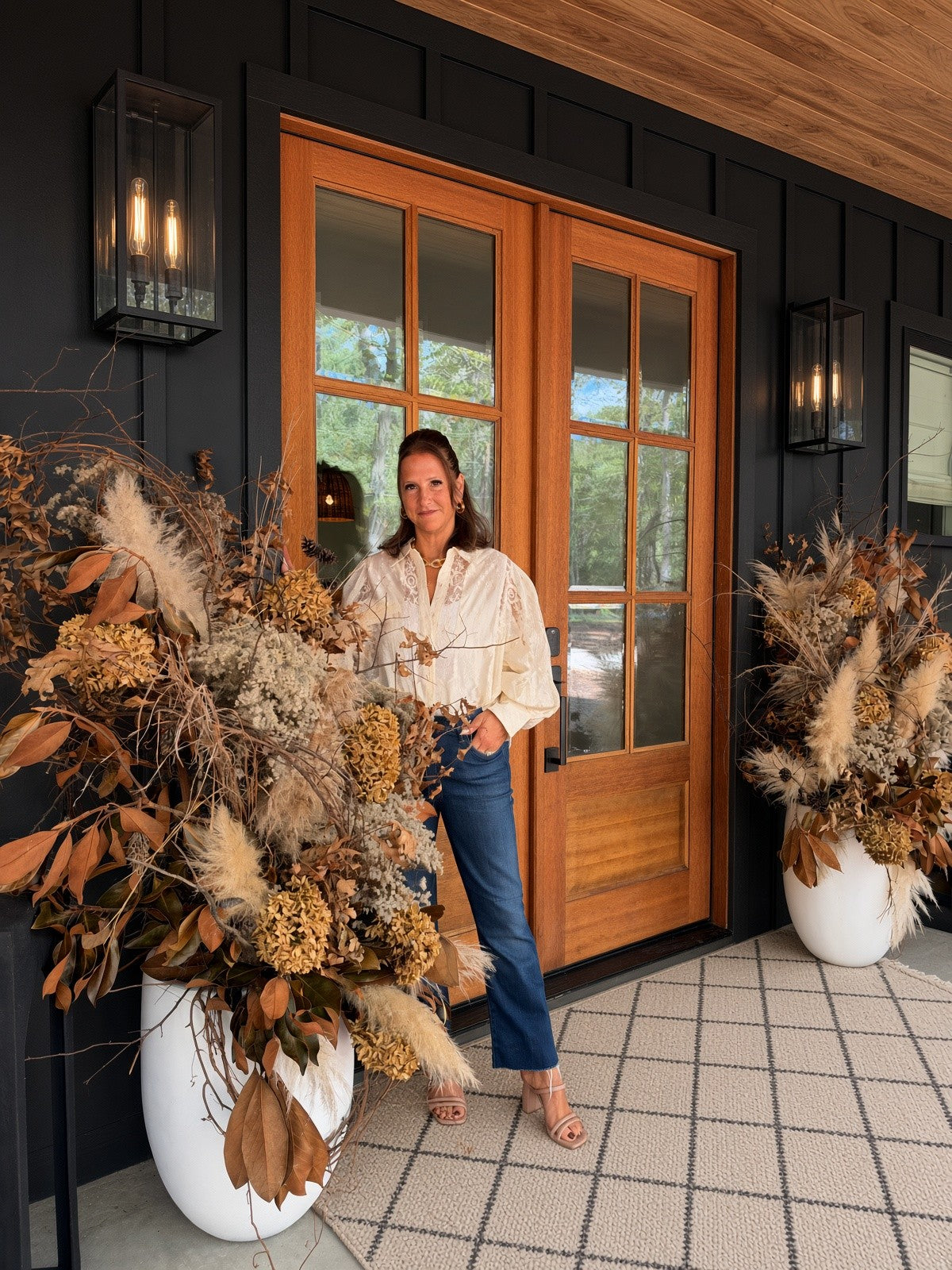 Heidi on a porch beside tall autumn planters at wood double doors
